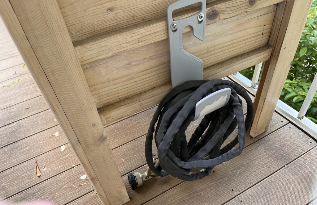 black hose on a hook attached to a planter box for watering deck garden plants